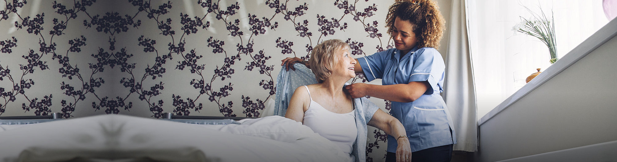 caregiver assists the elderly woman to dress up